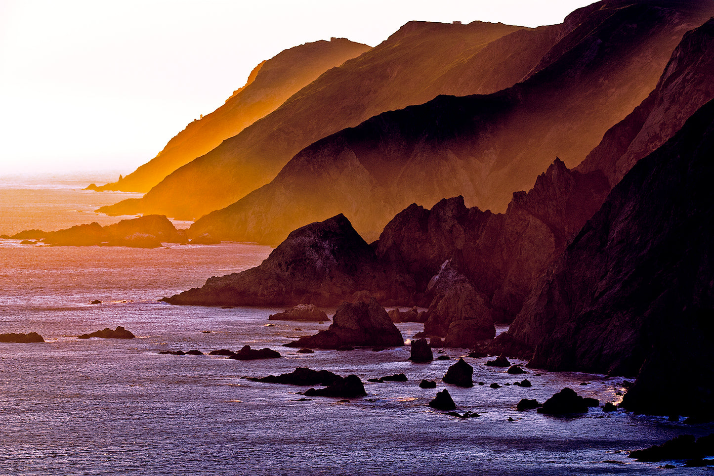 Sunset light spills across rugged coastal headlands at the southern tip of Point Reyes Peninsula in late winter, casting golden hues over cliffs and ocean.