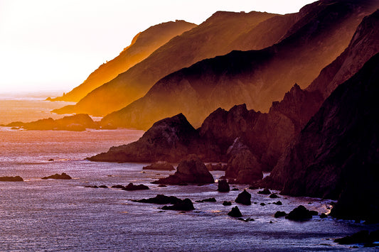 Sunset light spills across rugged coastal headlands at the southern tip of Point Reyes Peninsula in late winter, casting golden hues over cliffs and ocean.