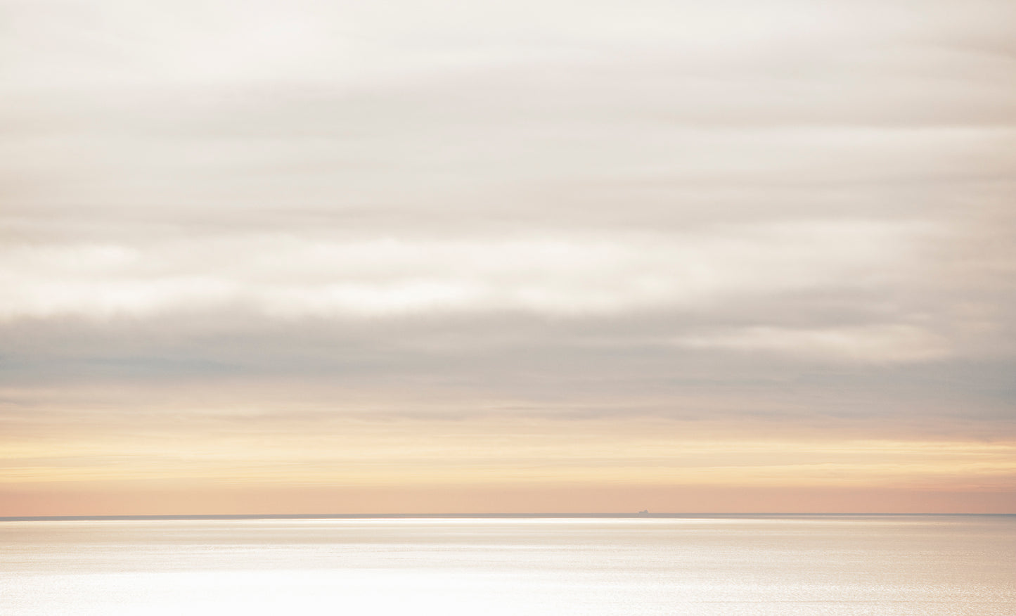 A soft, muted seascape viewed from the top of Mt. Tamalpais on a winter day, with a distant container ship barely visible on the horizon beneath layered clouds and glowing light.