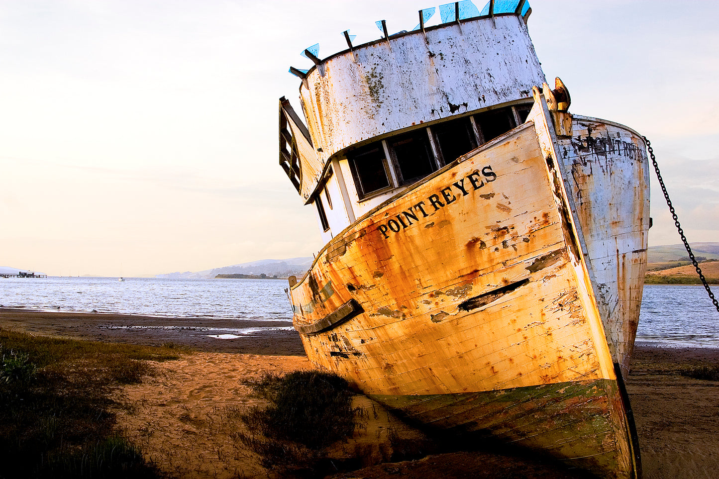 Weathered fishing boat named “Point Reyes” leaning on the shore of Tomales Bay, photographed over 20 years ago when its hull and cabin were still mostly intact, bathed in warm evening light.