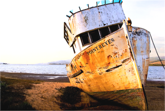 Weathered fishing boat named “Point Reyes” leaning on the shore of Tomales Bay, photographed over 20 years ago when its hull and cabin were still mostly intact, bathed in warm evening light.