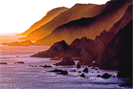 Sunset light spills across rugged coastal headlands at the southern tip of Point Reyes Peninsula in late winter, casting golden hues over cliffs and ocean.