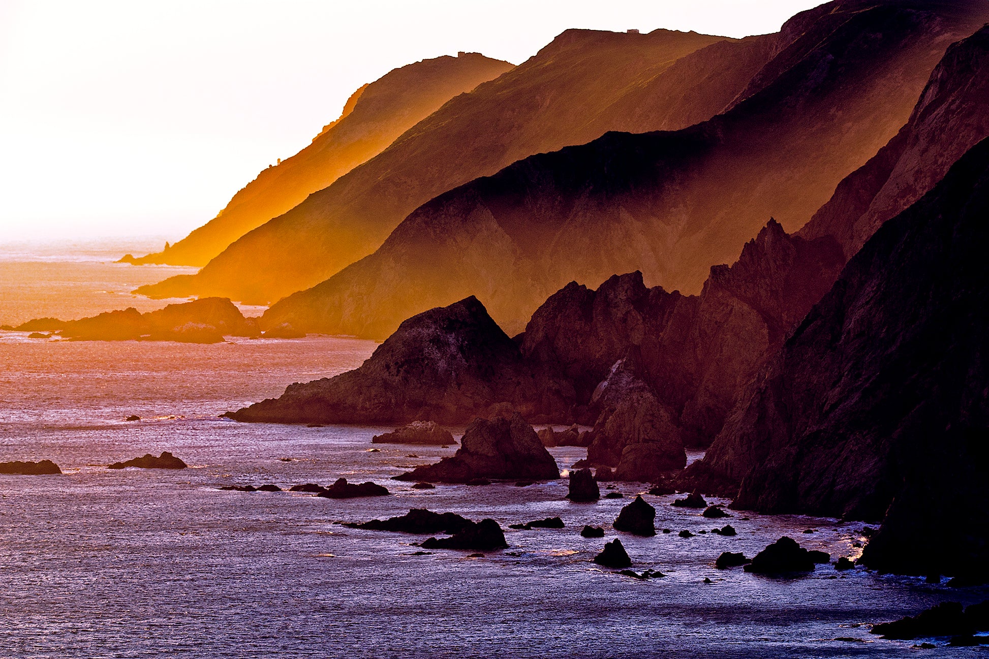 Sunset light spills across rugged coastal headlands at the southern tip of Point Reyes Peninsula in late winter, casting golden hues over cliffs and ocean.