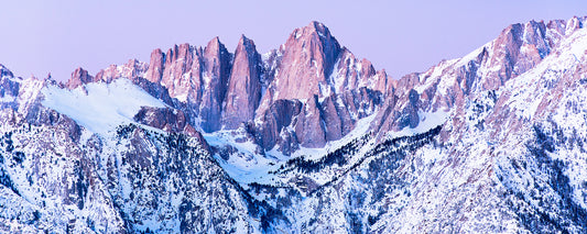 Snow-covered peaks of the Sierra Nevada glow with pink light at sunrise, viewed in winter from the Alabama Hills below Mount Whitney.