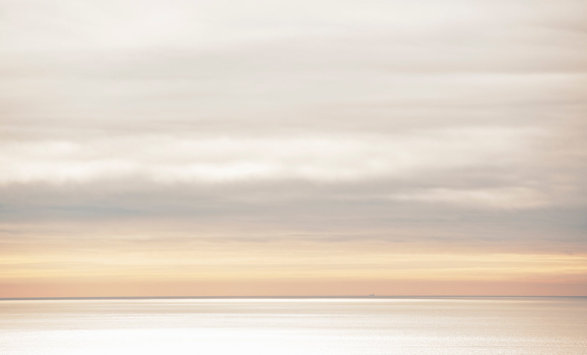 A soft, muted seascape viewed from the top of Mt. Tamalpais on a winter day, with a distant container ship barely visible on the horizon beneath layered clouds and glowing light.