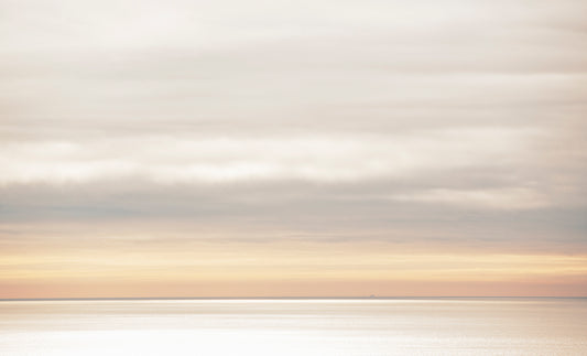 A soft, muted seascape viewed from the top of Mt. Tamalpais on a winter day, with a distant container ship barely visible on the horizon beneath layered clouds and glowing light.