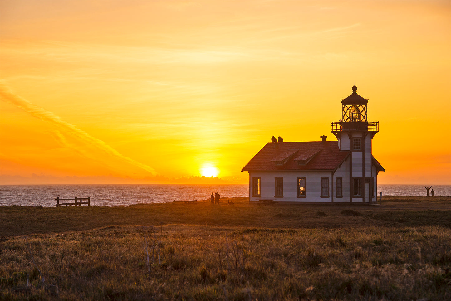 Silhouetted against a golden sunset, the Point Cabrillo Light Station stands along the Mendocino Coast as the sun dips into the Pacific Ocean, casting a warm glow over the horizon.