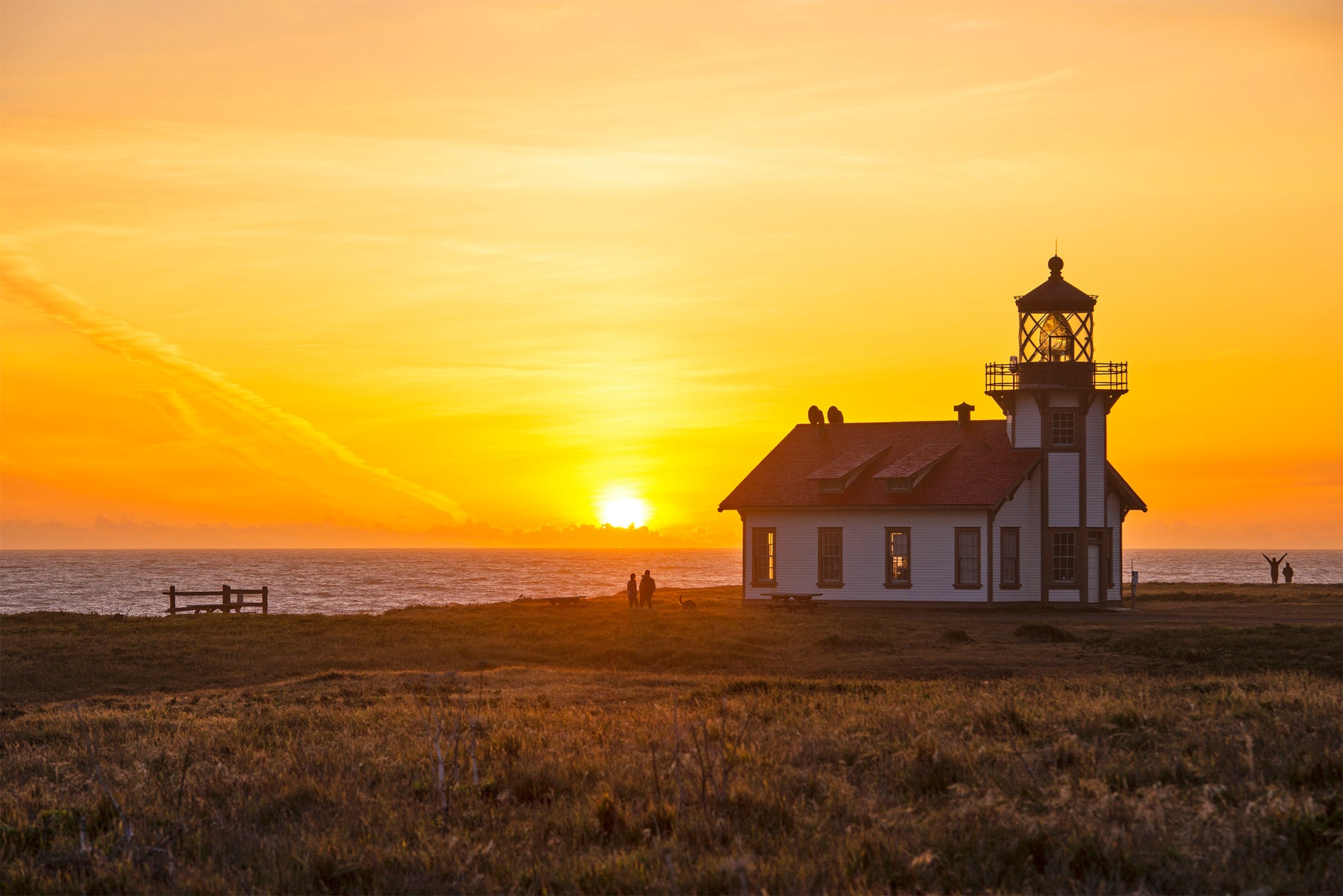 Silhouetted against a golden sunset, the Point Cabrillo Light Station stands along the Mendocino Coast as the sun dips into the Pacific Ocean, casting a warm glow over the horizon.