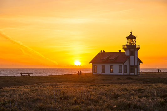 Silhouetted against a golden sunset, the Point Cabrillo Light Station stands along the Mendocino Coast as the sun dips into the Pacific Ocean, casting a warm glow over the horizon.