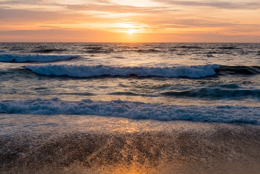 Golden sunset over breaking waves at North Beach in Point Reyes, with warm light reflecting off the wet sand and layers of surf rolling toward the shore.