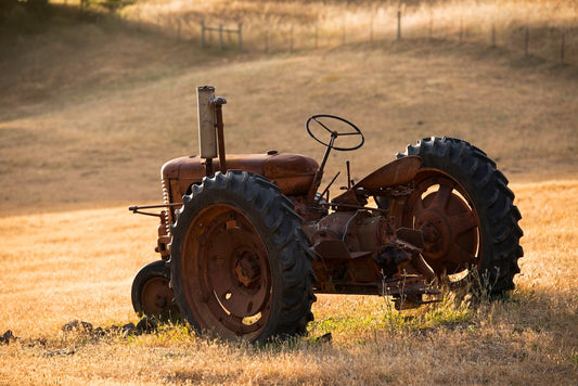 An old rusted tractor sits idle in a golden summer field along a remote backroad in Marin County, bathed in warm late afternoon light.