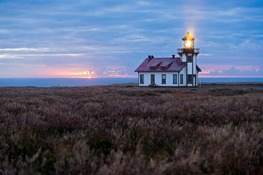 A serene summer sunset at Point Cabrillo Light Station on the Mendocino Coast, with the lighthouse beacon shining warmly as twilight colors reflect over the ocean; once featured as the homepage image for the California State Parks Association.