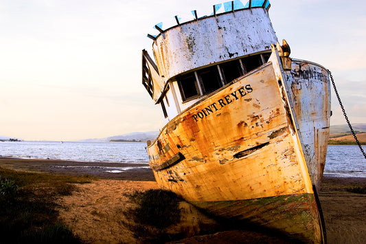Weathered fishing boat named “Point Reyes” leaning on the shore of Tomales Bay, photographed over 20 years ago when its hull and cabin were still mostly intact, bathed in warm evening light.