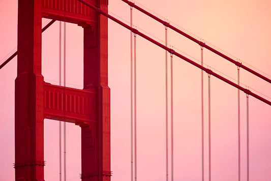 A close-up detail of the Golden Gate Bridge silhouetted against a pink and orange twilight sky on the summer solstice, captured while waiting for the strawberry moon to rise.
